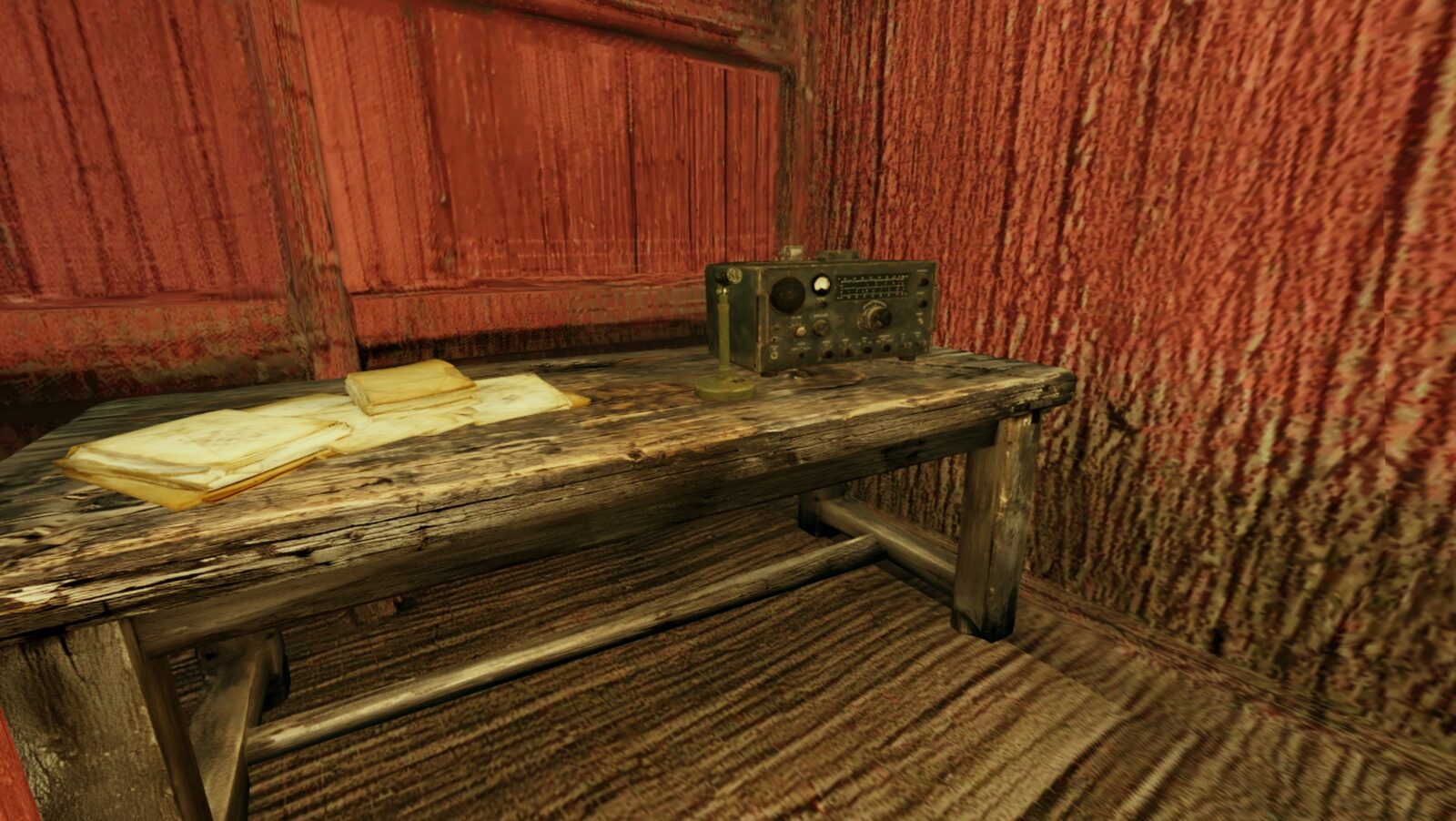 An old radio set and stacked papers on a wooden table against the barn's red wall